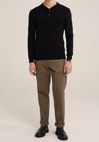 Svart långärmad polo med krage, med två knappar, tillsammans med beige chinos med uppvikt ärm och svarta ankelstövlar.