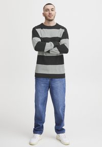 Pulover cu dungi gri și negre, cu textură în relief, de tip crew neckline, asortat cu blugi albaștri și adidași albi. Stil lejer.