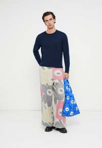 Námornícky úplet s dlhým rukávom v kombinácii s širokými šedými teplákmi so veľkými ružovými a čiernymi kvetinovými vzormi. Drží modrú vzorovanú tašku.