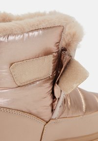 Svetlo ružová, prešívaná kožená čižma s kožušinovou podšívkou, suchý zips a hladká podrážka; lesklý povrch s minimálnymi prešívacími detailmi.