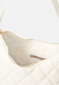 Quilted white handbag with a gold zipper and a smooth inner lining. Features a label that reads "ANNA FIELD" inside.