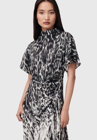 Vestido en blanco y negro con un diseño fluido de estampado animal. Presenta un cuello alto, mangas cortas y detalles de fruncido en los laterales. Textura suave.