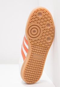 Adidas-sneakersula med en texturerad gummidesign i orange och beige, med tre orange ränder på sidan och logodetalj.