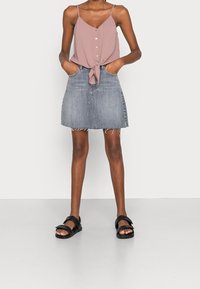 Haut caraco rose avec détails à boutons, noué à la taille, associé à une jupe en denim gris à ourlet effiloché et des sandales noires.