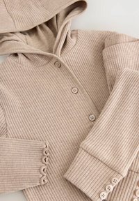Beige stickad hoodie med ribbad struktur, med knappframsida och scallopade muddar. Slätt tyg med huva för extra värme.