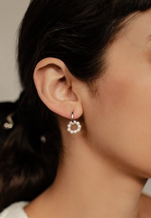 Boucle d'oreille en perles avec un fermoir en métal argenté, présentant un design circulaire orné de petites perles blanches disposées en motif.