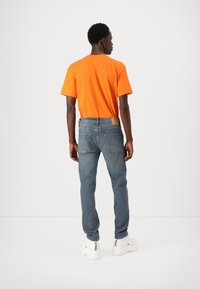 Camiseta de algodón naranja, jeans de mezclilla azules y zapatillas blancas. Los jeans tienen bolsillos traseros y una etiqueta de cuero en la cintura.