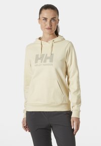 Sudadera color crema hecha de tela suave, con un bolsillo frontal y un gran logo "HH" gris. Incluye cordones y puños de canalé.