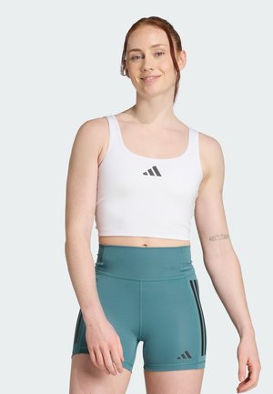 Hvit sporty crop top med svart logo, kombinert med høy midje teal shorts som har tre svarte striper på hver side.