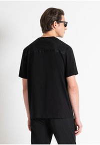 Camiseta negra con la parte trasera lisa y un panel superior trasero texturizado y con patrón. Mangas cortas y un corte relajado, fabricada con material ligero.