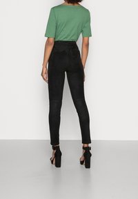 Svarta mockabyxor med en figursydd design, utrustade med elastisk midja och en smidig struktur, som matchar med svarta högklackade skor.