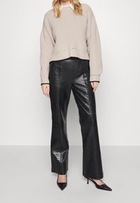 Beige geribde gebreide cropped sweater met een ruwe zijkant, gecombineerd met hooggewaiste zwarte faux leren broek met een krokodillenstructuur. Zwarte puntige hakken.