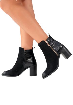 Bottines noires avec une combinaison de textures lisses et gaufrées crocodile, détail de zip sur le côté, et un talon bloc.