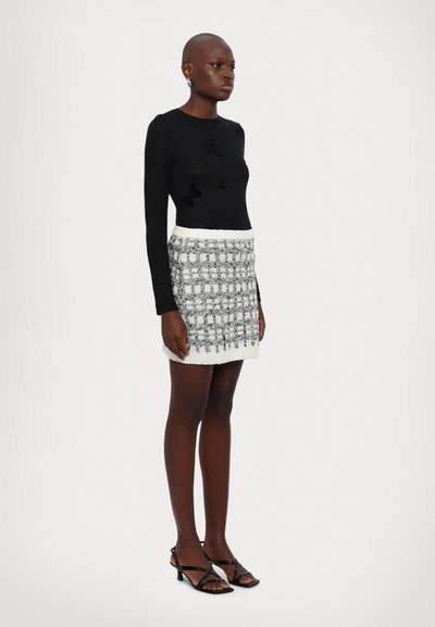 Black long-sleeve top with butterfly embroidery, paired with a white and gray patterned knit skirt. Model wears black strappy heeled sandals.