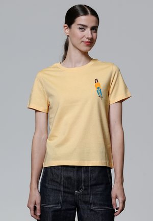Gelbes Baumwoll-T-Shirt mit kurzen Ärmeln, das auf der linken Brustseite eine kleine Grafik einer Person auf einem Fahrrad zeigt.