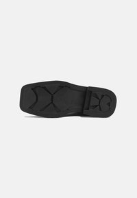 Suela de zapato de goma negra con un diseño plano, que presenta surcos de tracción con patrones y un ligero tacón. Sin texturas ni acentos adicionales.
