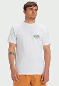 Camiseta branca de manga curta feita de algodão, com um logótipo circular e colorido no peito e um decote redondo. Design simples e clássico.