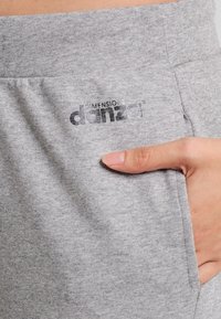 Szare spodnie dresowe z miękkiego materiału, z boczną kieszenią i nadrukowanym logo "DIMENSIONE DANZA" w pobliżu talii.