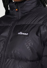 Black puffer jacket with a high collar, featuring subtle embossed branding and a fabric logo patch, zip closure, and textured surface.