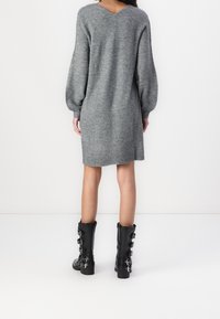 Szara dzianinowa sukienka z dekoltem w serek i bufiastymi rękawami, połączona z czarnymi kozakami do kolan z klamrami. Gładka tekstura, casualowy styl.