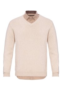 Beige V-hals trui gemaakt van zacht materiaal, met lange mouwen en geribde manchetten, gelegd over een lichtbruine overhemd met kraag.