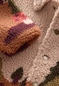 Fuzzy, textured fabric in shades of beige, orange, and purple with an abstract pattern. Features visible buttons for closure.