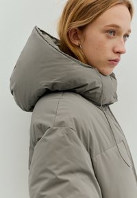 Grijze pufferjas met een grote, opvouwbare capuchon, een gladde textuur en een minimalistisch ontwerp met weinig zichtbaar beslag.