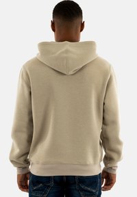 Sudadera beige con capucha con cordón, puños y dobladillo acanalados. Textura suave, corte relajado y sin patrones ni logotipos visibles.