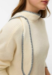 Krēmkrāsas džemperis ar augstu apkakli, ribotu faktūru un viļņainu pelēku akcentu gar plecu un apkakles malām.
