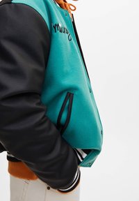 Veste universitaire avec un corps en laine bleu sarcelle, des manches synthétiques noires, un cordon orange et des poignets côtelés rayés. Comprend des poches latérales et des lettres.