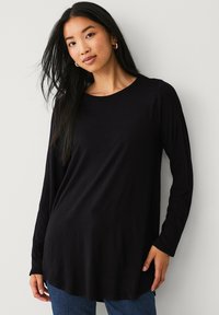 Haut noir à manches longues avec un col rond, en tissu doux, présentant une coupe ample qui dépasse les hanches. Design simple sans motifs.