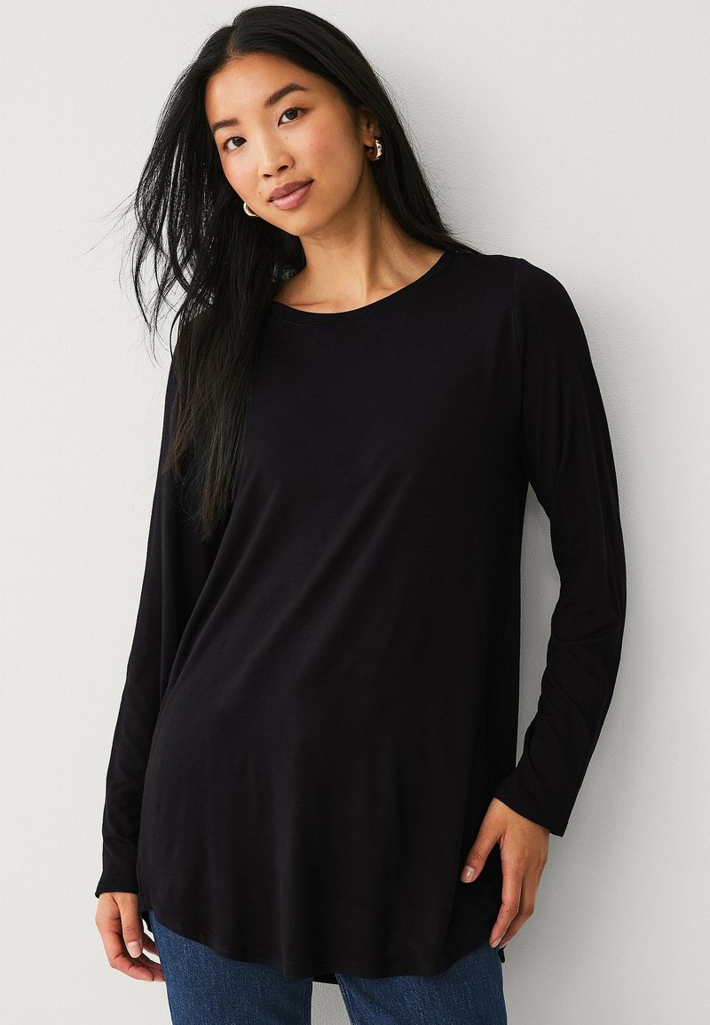 Haut noir à manches longues avec un col rond, en tissu doux, présentant une coupe ample qui dépasse les hanches. Design simple sans motifs.