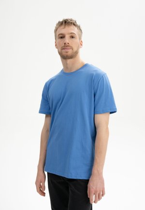 Blauwe katoenen t-shirt met korte mouwen, ronde hals, rechte snit en minimale stikseldetails, gedragen met zwarte broeken.