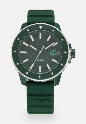 Montre à bracelet en silicone vert avec un cadran rond vert, index horaires blancs, accents argentés et logo Lacoste. Résistante à l'eau jusqu'à 10 bars.