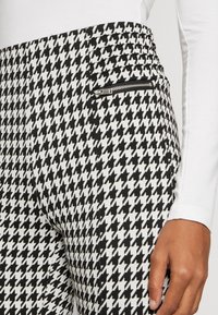 Zwart-witte houndstooth-patroon broek met een gestructureerde afwerking, voorzien van een ritszak en een getailleerd silhouet.