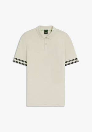 Polo de color beige claro hecho de tela suave. Cuenta con mangas cortas con detalles a rayas en blanco y negro en los puños. Cuello con dos botones.