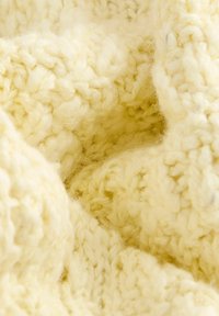Gros plan d'un tissu tricoté doux, épais, de couleur crème montrant un fil épais et des motifs de points texturés.