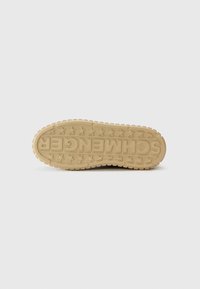 Semelle de chaussure en caoutchouc beige avec une surface texturée, featuring une marque en relief et des motifs d'étoiles. Forme arrondie avec un design de semelle proéminent.