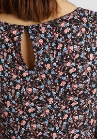 Top floral noir avec de petites fleurs roses et bleues. Doté d'un col rond et d'un détail en forme de trou de serrure à l'arrière, fabriqué en tissu léger.