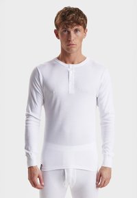 Hvit langermet skjorte laget av lett materiale med rund hals og tre knapper. Myk tekstur og tettsittende design.