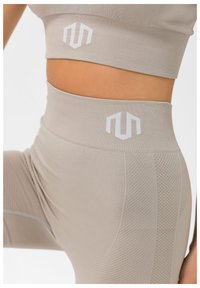 Beige treningstøysett med en ribbestrikket sport-bh og høyt midjeleggings med teksturerte paneler og hvite logo detaller.
