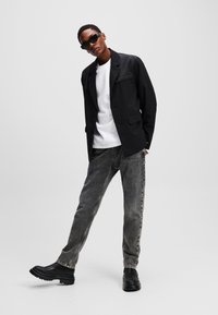 Black jacket with a textured finish, white t-shirt underneath, gray jeans, and black chunky boots. The figure poses in a modern style.