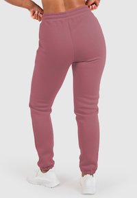 Rosa Baumwoll-Sweathose mit einem elastischen Bund und Knöchelabschlüssen, die eine glatte Textur aufweisen. Getragen mit weißen Sportschuhen.