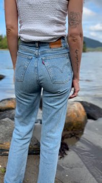 Jeans de ganga azul claro com cintura alta e corte reto. Apresentam bolsos traseiros e um patch de couro na cintura. Sem padrões visíveis.