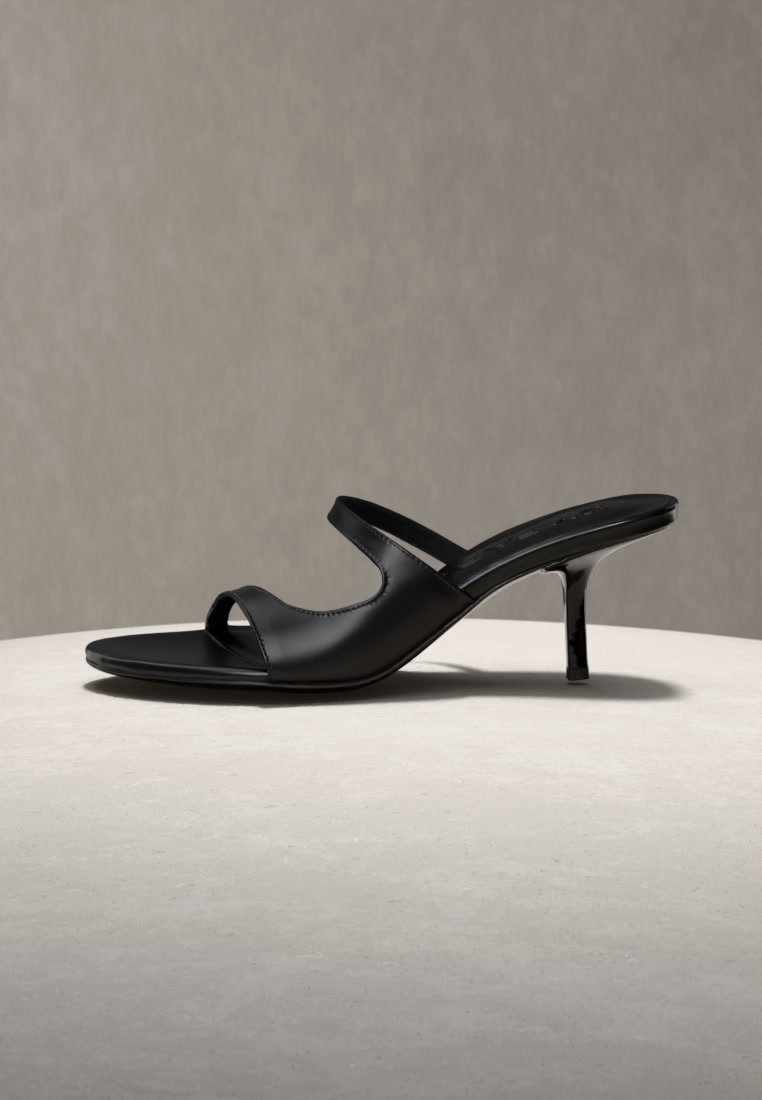 Black leather open-toe mule with two straps and a slim mid-height stiletto heel on a light stone surface.