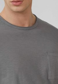 Graues Baumwoll-T-Shirt mit Rundhalsausschnitt, kurzen Ärmeln und einer kleinen Brusttasche mit feiner Textur.