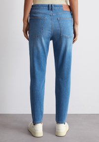 Hele sinised denim püksid sirge lõikega, kahe tagataskuga ja pruuni nahkplekkiga vöökoht. Sile tekstuur.
