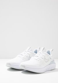 Białe buty sportowe z teksturowanej siateczki, z wyściełaną podeszwą, jasnoniebieskimi akcentami i wyraźnym logo po boku.