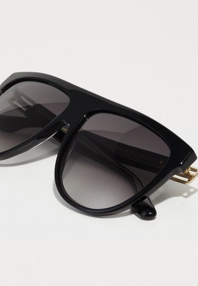 Óculos de sol oversized pretos com lentes cinzentas. Feitos de plástico brilhante, com detalhes em dourado nas dobradiças. Formato angular com hastes grossas.