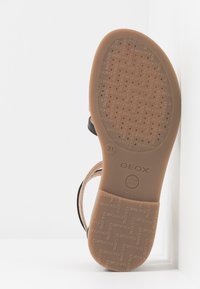 Svart sandal med en lädrom brun texturerad sula, med mönstrade spår och varumärkeslogotyp. Designad för andningsförmåga.